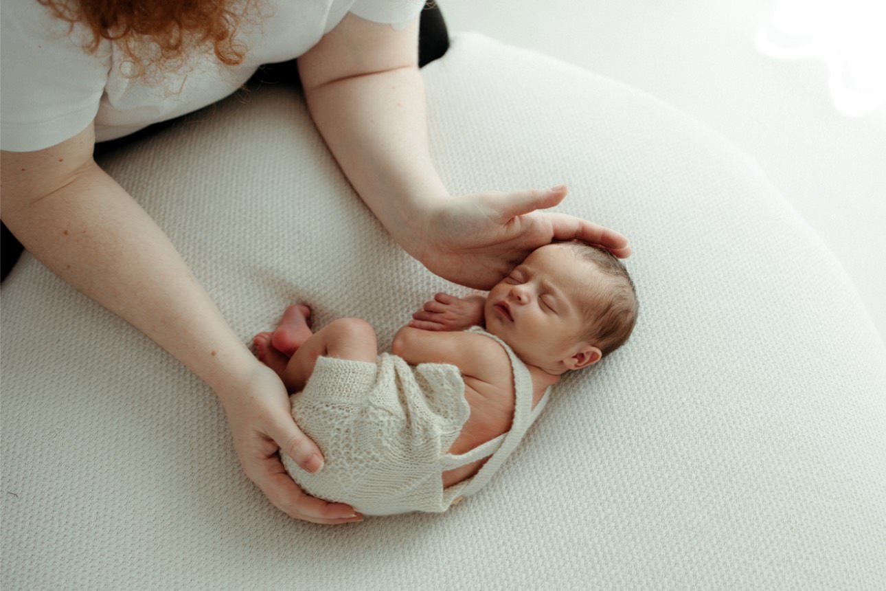 A baby is placed on a beanbag as a photographer's hands pose the baby.