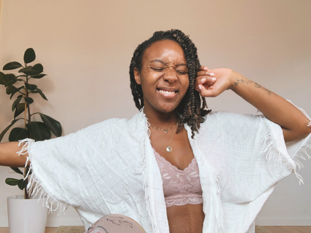 Menstrual cycle and business Natalie Martin, black woman, sits with her eyes shut but smiling in white oversized shirt and bra